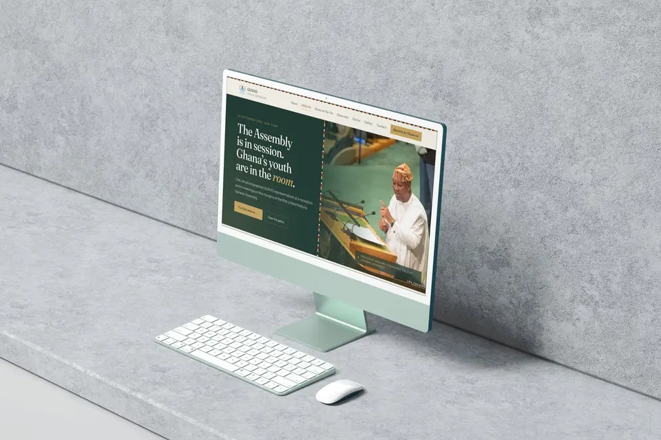 Green iMac with a keyboard and mouse on a concrete ledge, showing the GUNYO UNGA 81 page, The Assembly is in session. Ghana’s youth are in the room., beside a photograph of a speaker at the General Assembly podium.